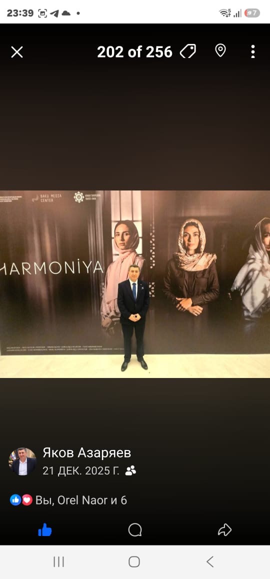 Яков Азаряев в тёмном костюме у большого баннера с надписью HARMONIYA.