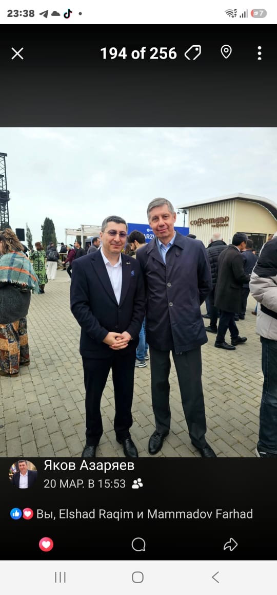 Двое мужчин в тёмных пиджаках стоят на мощёной площадке под открытым небом.